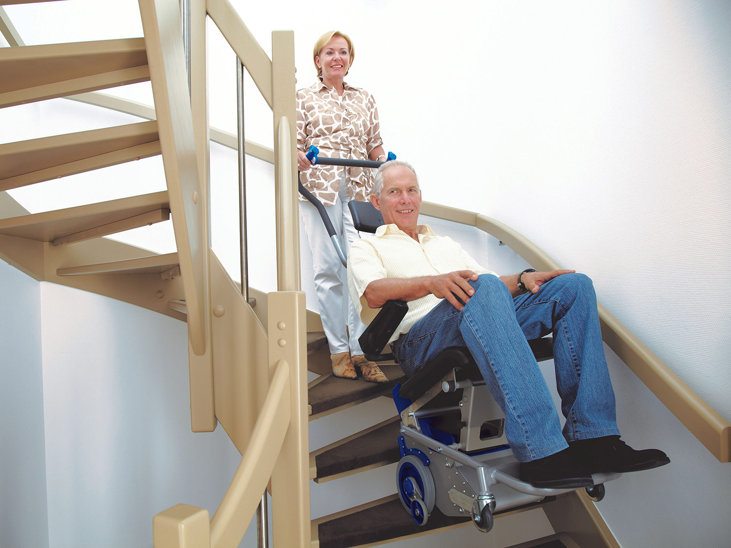 Foto einer Frau die einen älteren Mann in einem Rollstuhl mit einer Treppenraupe die Treppe hochbefördert
